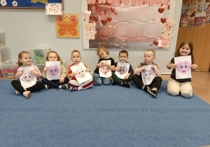 Dzieci na dywanie trzymają przed sobą swoje rysunki