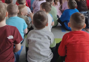 Dzieci siedzą na dywanie i oglądają prezentację multimedialną o bezpieczeństwie w sieci