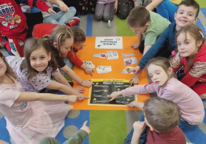 Dzieci siedzą dookoła wykonanego plakatu i pokazują obrazki