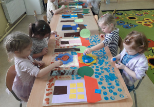 Dzieci przy stolikach stemplują okrągłymi pomponami makietę geometrycznej wioski.