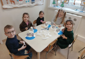 Dzieci siedzą przy stoliku i tworzą zimową krainę Inuitów.