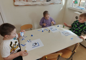 Dzieci siedzą przy stoliku i układają pocięte obrazki w całość.