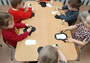 Dzieci przy stoliku wykonują pracę plastyczną - pingwina