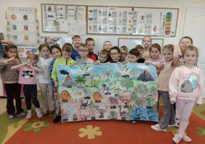 Przedszkolaki prezentują wykonany plakat parku dinozaurów.