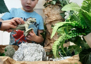 Chłopiec bawi się figurkami dinozaurów przy makiecie parku jurajskiego.