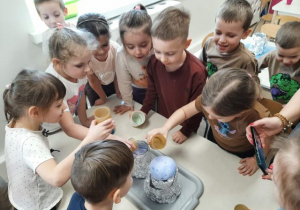 Dzieci stoją dookoła stolika i obserwują ekseryment z erupcją wulkanu.