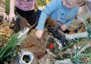 Chłopiec z dziewczynką bawią się figurkami dinozaurów przy makiecie parku jurajskiego.