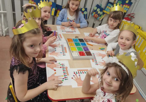 Dziewczyny siedzą przy stoliku w koronach na głowie i wyklejają plasteliną