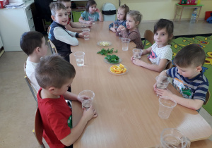 Dzieci przy stolikach przygotowują się do wykonania wody smakowej.