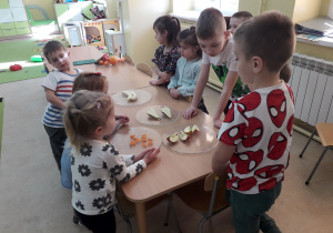 Dzieci przy stolikach przeliczają i nazywają owoce.