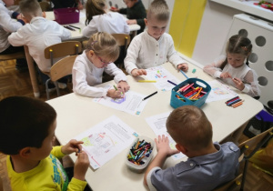 Dzieci siedzące przy stolikach i kolorujące obrazki