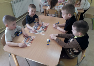 Chłopcy przy stoliku składają w całość plakat "W marcu jak w garncu".