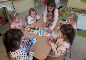 Dziewczynki przy stoliku składają w całość plakat "W marcu jak w garncu".