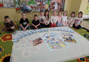 Dzieci na dywanie prezentują wykonane przez siebie plakaty "W marcu jak w garncu".