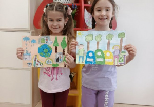 Dziewczynki prezentują prace plastyczne na konkurs.