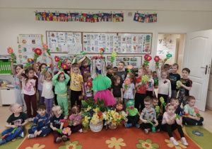 Dzieci trzymają kolorowe kwiatki i pozują do zdjęcia z marzanną.