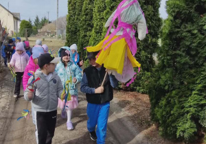 Dzieci idą w parach na spacer. Dziecko trzyma Marzannę.