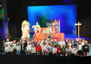 Dzieci stoją pod sceną i pozują do zdjęcia z aktorami.