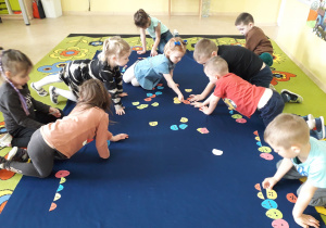 Dzieci podczas zabawy matematycznej na dywanie dopasowują połówki pisanek.