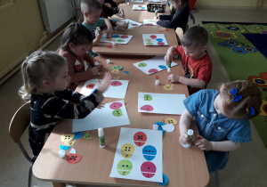Dzieci przy stolikach dopasowują i naklejają połówki pisanek.