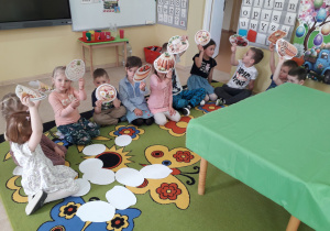 Dzieci na dywanie podczas zabawy tematycznej losują sylwety potraw wielkanocnych, podając jej nazwę.