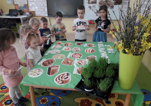 Dzieci kartonikami z nazwami podpisują potrawy wielkanocne ułożone na stole.