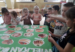 Dzieci kartonikami z nazwami podpisują potrawy wielkanocne ułożone na stole.