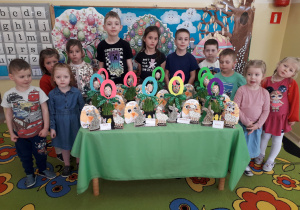 Dzieci stoją wokół stołu prezentują wykonane stroiki wielkanocne.
