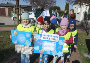 Przedszkolaki w drodze na Niebieskie Igrzyska. Dziewczynki trzymają plakaty tematyczne.