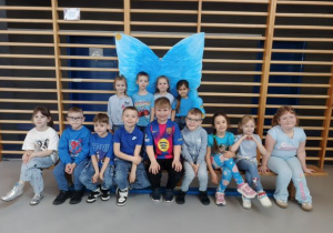 Przedszkolaki pozują do zdjęcia grupowego na tle niebieskich skrzydeł.