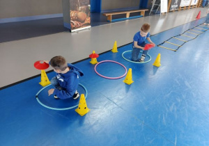 Chłopcy przekładają krążki na pachołkach.