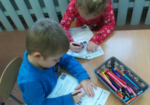 Dzieci przy stoliku kolorują ilustracje.