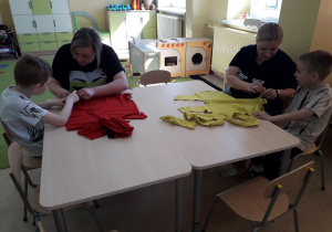 Warsztaty ekologiczne. Mamy z dziećmi przy stolikach podczas wykonywania torby ekologicznej na zakupy z niepotrzebnej koszulki.