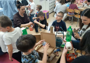 Dzieci razem z rodzicmi siedzą przy stoliku i tworzą eko zabawki.