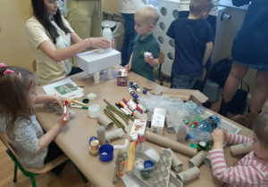 Dzieci razem z rodzicmi siedzą przy stoliku i tworzą eko zabawki