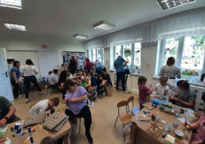 Dzieci razem z rodzicmi siedzą przy stoliku i tworzą eko zabawki