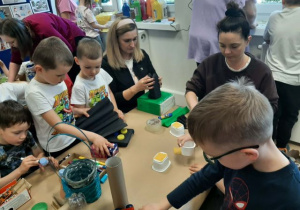 Dzieci razem z rodzicmi siedzą przy stoliku i tworzą eko zabawki
