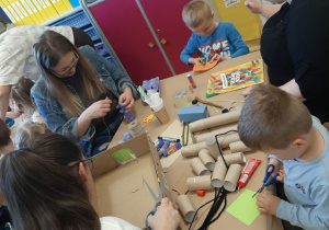 Dzieci razem z rodzicmi siedzą przy stoliku i tworzą eko zabawki