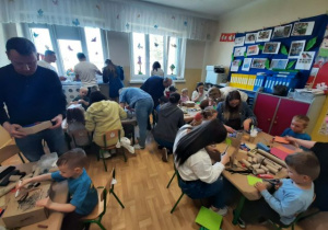 Dzieci razem z rodzicmi siedzą przy stoliku i tworzą eko zabawki