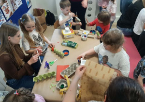 Dzieci razem z rodzicmi siedzą przy stoliku i tworzą eko zabawki