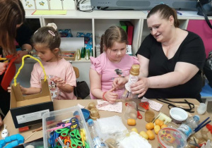 Dzieci razem z rodzicmi siedzą przy stoliku i tworzą eko zabawki