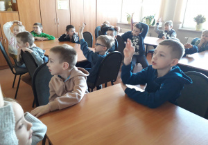 Dzieci siedzą przy stolikach w szkolnej bibliotece.