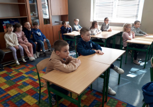 Dzieci siedzą w ławkach w sali lekcyjnej.