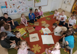 Przedszkolaki siedzą w kole na dywanie, w środku leżą torby na zakupy.