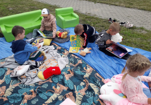 Dzieci w plenerowej strefie czytelniczej oglądają różne książeczki.