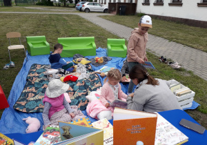 Dzieci w plenerowej strefie czytelniczej oglądają różne książeczki.