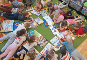 Dzieci z grupy 3,4-latków leżą na brzuszkach na dywanie i oglądają książeczki.