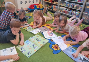 Dzieci leżą na dywanie i oglądają swoje ulubione książeczki.