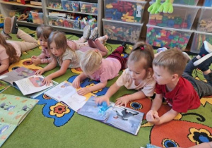 Dzieci leżą na dywanie i oglądają swoje ulubione książeczki.