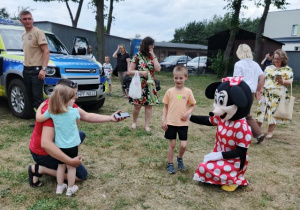 Dzieci z rodzicmi robią zdjecia z dużą maskotką Myszki Minnie.